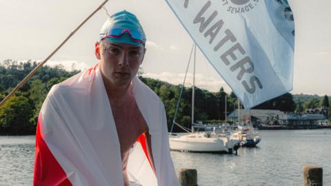 Hector Pardoe looks from boat on lake on with flag draped round him