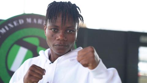 MMA fighter Juliet Ukah wears a white top and holds up two fists as she looks straight ahead
