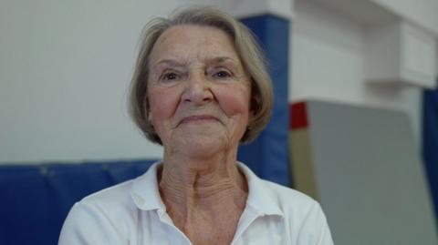 Head and shoulder shot of octogenarian Anita Waters. She looks younger than her years, with light blonde bobbed hair and wearing a white open-necked shirt.
