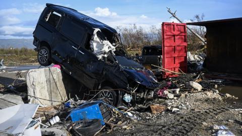 A battered car juts out of debris from Hurricane Melissa. 