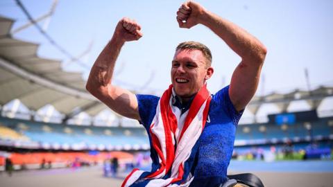 Nathan Maguire has a union jack flag draped around his neck and holds up his arms