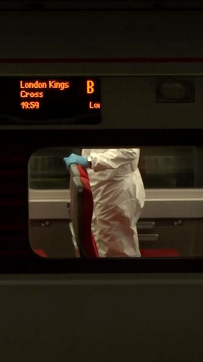 A view of inside a train from the outside. A man in a white forensics suit and a blue glove, standing up.
