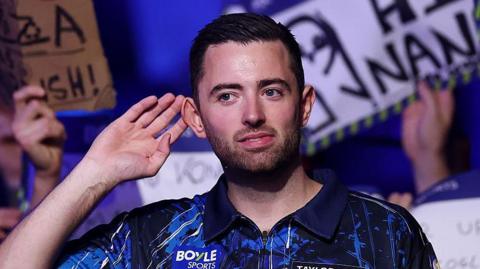 Luke Humphries cups his ear to the fans