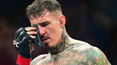 Tom Aspinall dabs his eye after suffering an eye poke during his fight with Cyril Gane at UFC 321