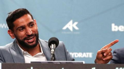 Amir Khan laughs and points his finger speaking at a news conference